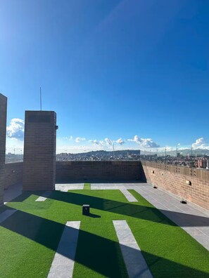 A rooftop terrace with artificial grass, a brick wall, and a view of a cityscape. - Modern Suite | Santa Fe Clinic | Usaquén (Bogotá)