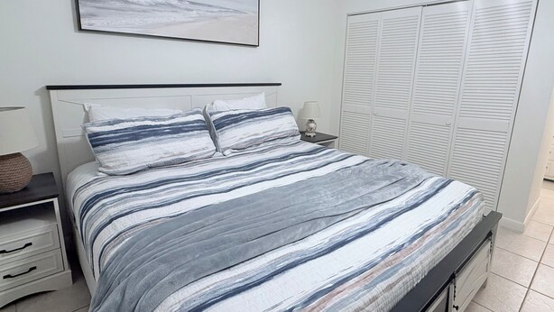 A bedroom with a bed, a nightstand, a lamp, a bedside table, a wardrobe, and a framed picture on the wall. - Sun&Sand Oasis - Beach Front - 2/2 Condo - Next to Heated Pool - Ground Floor (St. Augustine)