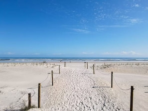 Ein sandiger Strand mit blauem Himmel und weiter Meer im Hintergrund.