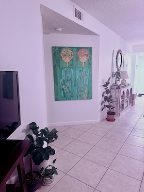 A hallway with a TV, artwork, potted plants, and a console table. - Sun&Sand Oasis - Beach Front - 2/2 Condo - Next to Heated Pool - Ground Floor (St. Augustine)