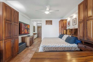 Quarto com cama, armários de madeira, ventoinha no teto e piso ladrilhado.