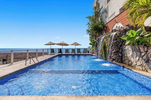 Piscina com vista para o oceano, rodeada por espreguiçadeiras e guarda-sóis.