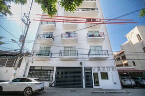 A multi-story building with balconies, a garage entrance, and visible power lines. - Casa Lluvia Retreat • Rooftop Infinity Pool (Puerto Vallarta)