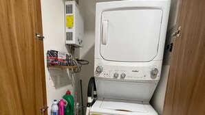 Ett litet och praktiskt tvättrum med tvättmaskin och torktumlare, en liten hylla med rengöringsmedel och en ventilationsöppning i väggen.