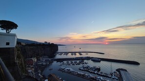 A coastal marina with boats docked, a sunset in the background, and a cliffside building. - Unit 8 - Bright Apartment Near the Beach & Downtown (Piano di Sorrento)