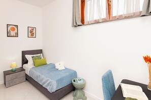 Um quarto moderno com cama, mesa de cabeceira, abajur e um pequeno banquinho verde.