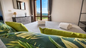 Ein Hotelzimmer mit Bett, Nachttisch, Lampe, einem Glas Wasser und Blick auf den Ozean.
