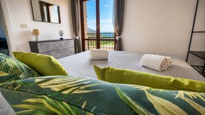 A hotel room with a bed, a nightstand, a lamp, a glass of water, and a view of the ocean. - Unit 8 - Bright Apartment Near the Beach & Downtown (Piano di Sorrento)