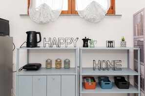 Quarto com cozinha compacta, cafeteira, chaleira, telefone e recipientes de armazenamento.