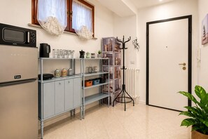 Een keuken met een koelkast, magnetron en een plank met potten. Er is een radiator en een deur met een sleutelgat.