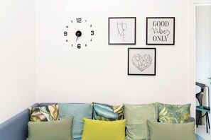 A living room with a clock, framed artwork, and a couch with patterned cushions. - Unit 8 - Bright Apartment Near the Beach & Downtown (Piano di Sorrento)