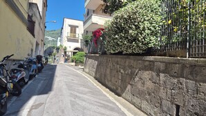 Eine schmale Gasse mit abgestellten Rollern, einer Steinmauer und Häusern mit Balkonen.