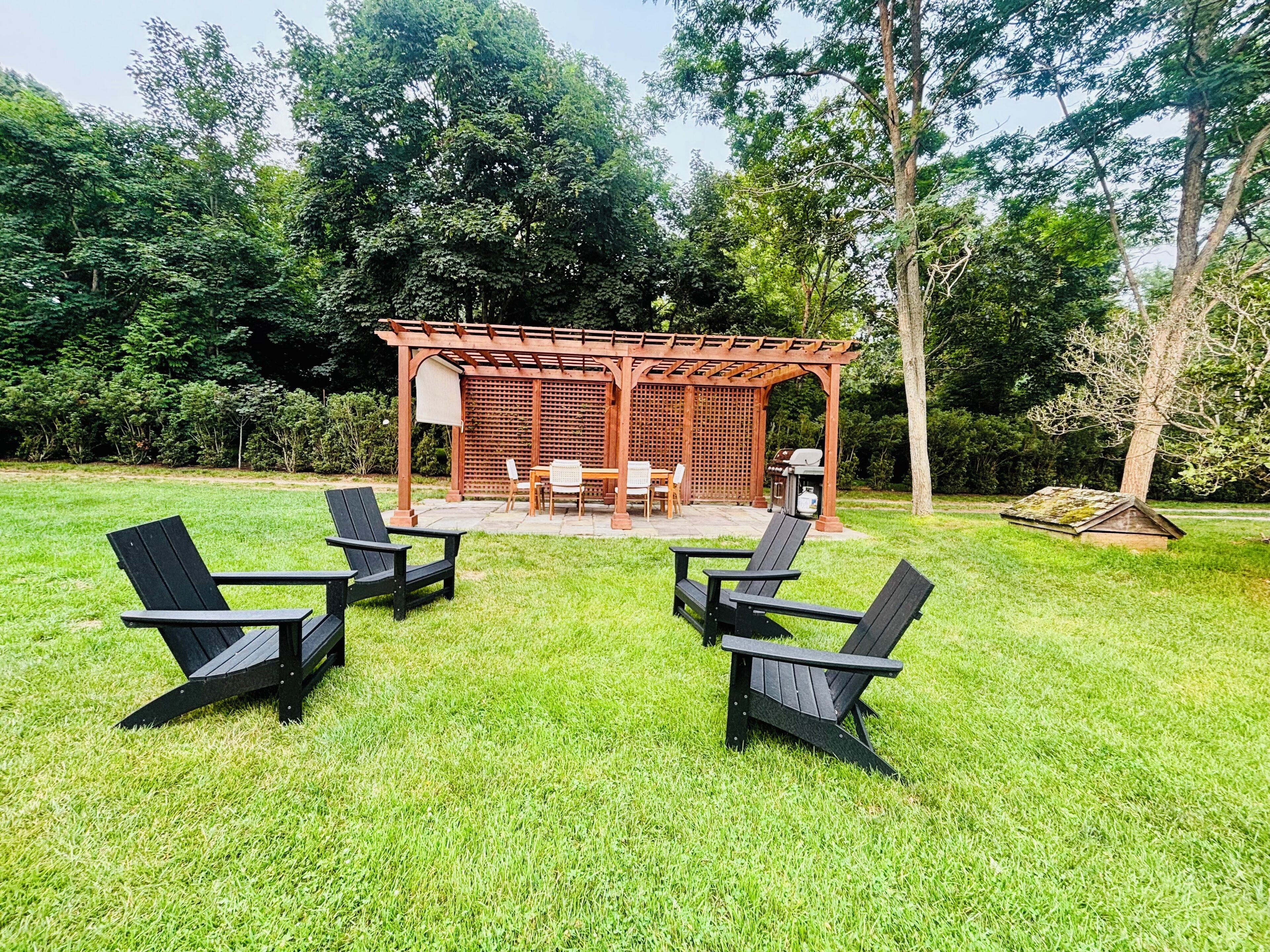 A gazebo with a table and chairs, surrounded by a grassy lawn with Adirondack chairs.