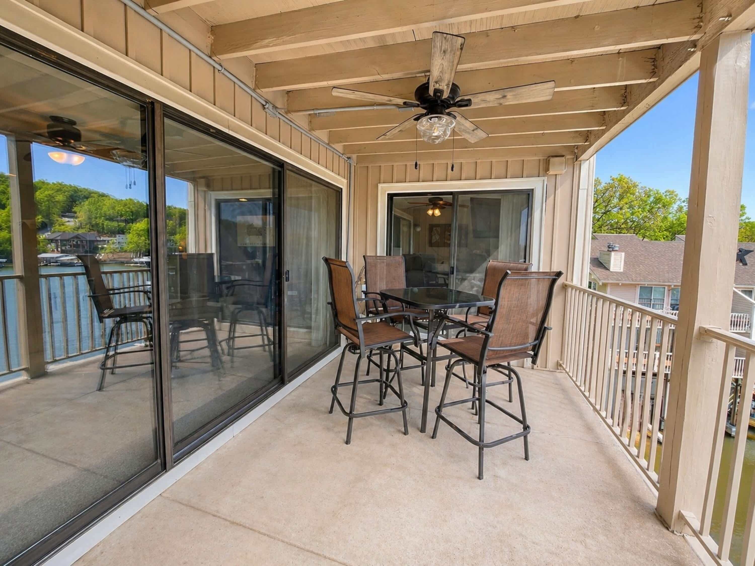 Une terrasse couverte avec une table et des chaises, un ventilateur de plafond et une vue sur une étendue d’eau.