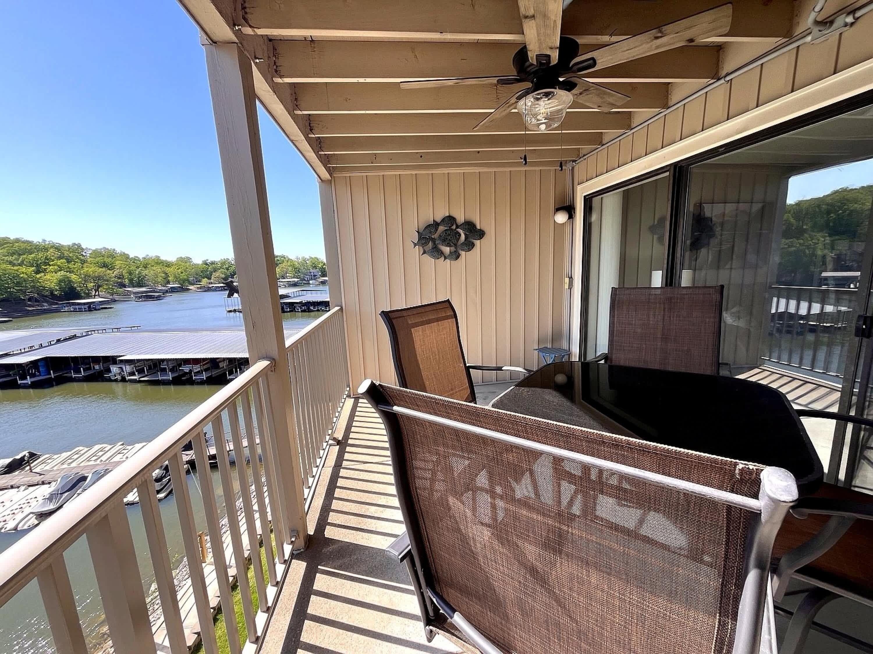 A balcony with a view of a dock and boats, a ceiling fan, and a glass door leading to an outdoor area.