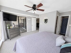 A bedroom with a bed, a dresser, a ceiling fan, a TV, and a door leading to a balcony. - Serenity Pointe Boat Slip (Osage Beach)