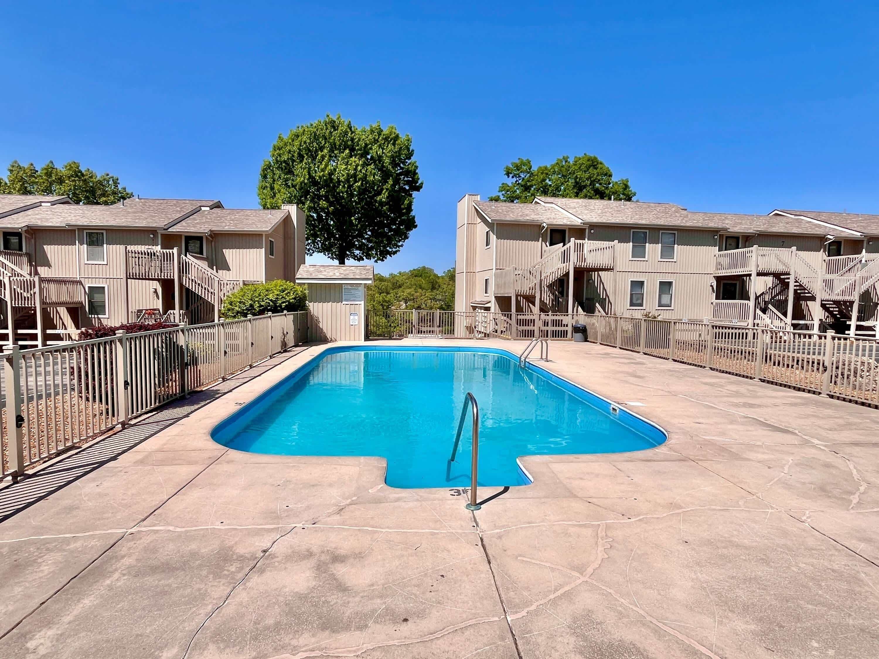 A rectangular swimming pool with a metal ladder in the center, surrounded by a concrete deck.