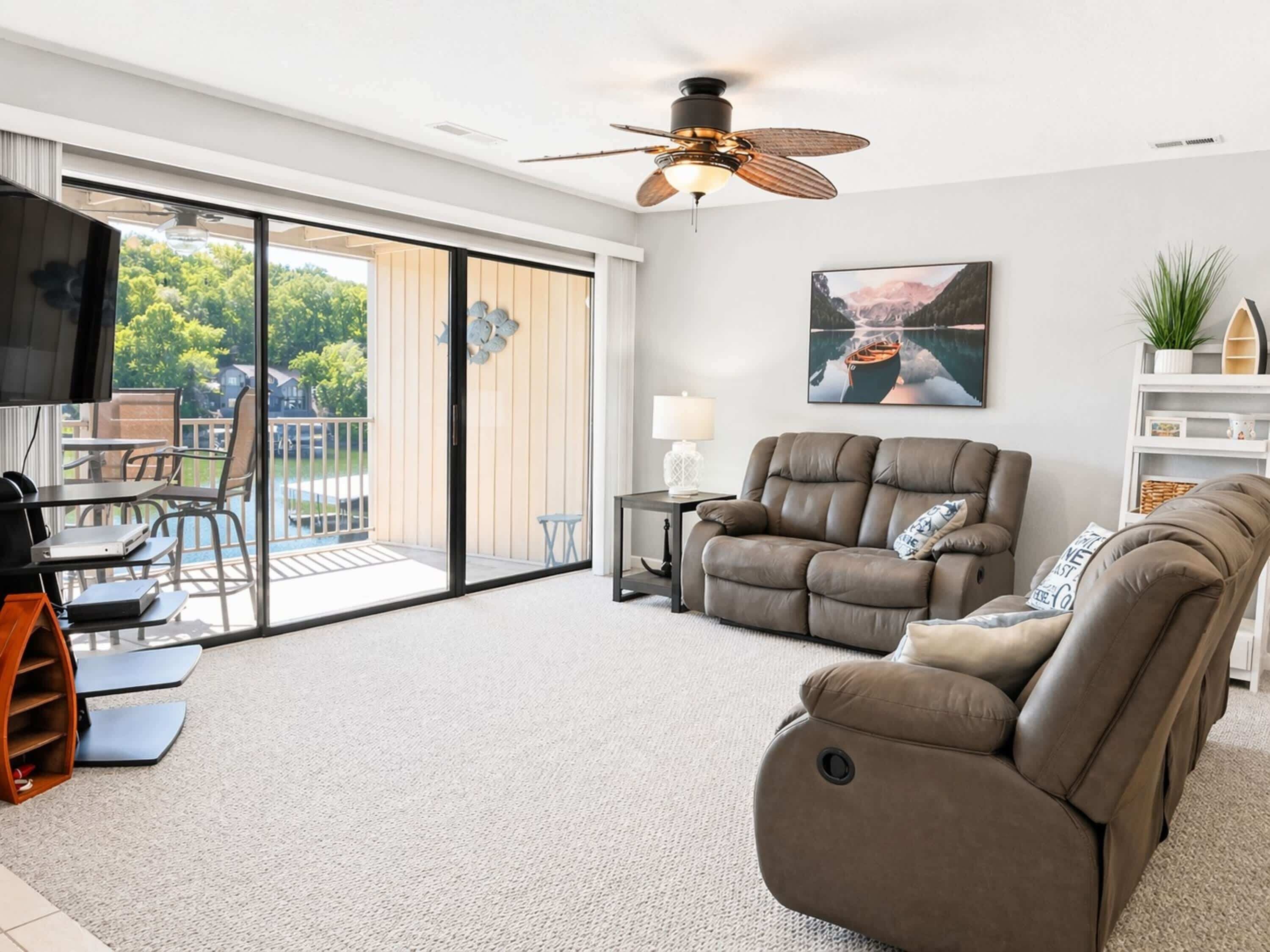 A modern living room with a sofa, a TV, a ceiling fan, and a sliding glass door leading to an outdoor area.