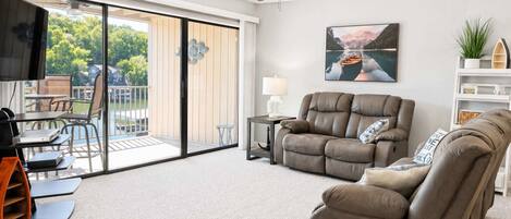 A modern living room with a sofa, a TV, a ceiling fan, and a sliding glass door leading to an outdoor area.