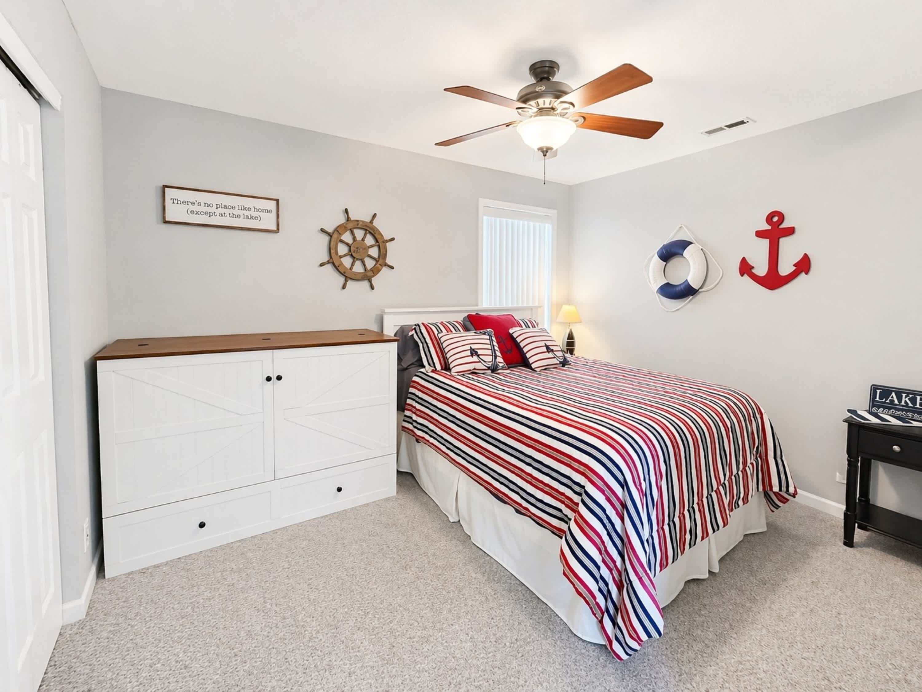 Un dormitorio con cama, ventilador de techo, decoración náutica en la pared, timón de barco y una cita enmarcada.