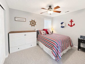 Ein Schlafzimmer mit einem Bett, einem Deckenventilator, einer Wanddekoration mit Anker, einem Steuerrad und einem gerahmten Zitat.
