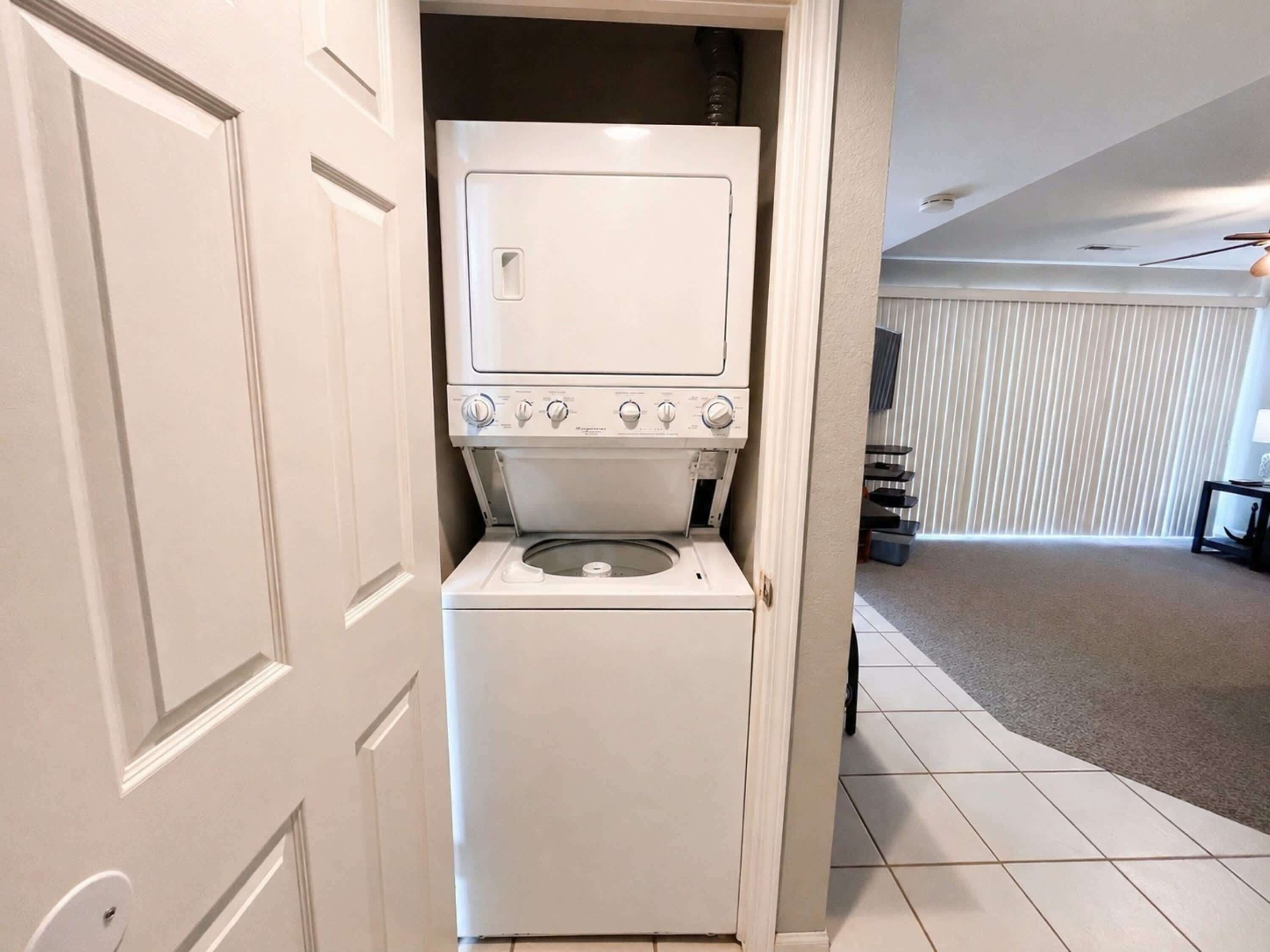 A compact washer and dryer unit in a hallway with a door leading to another room.