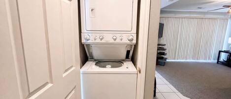 A compact washer and dryer unit in a hallway with a door leading to another room.