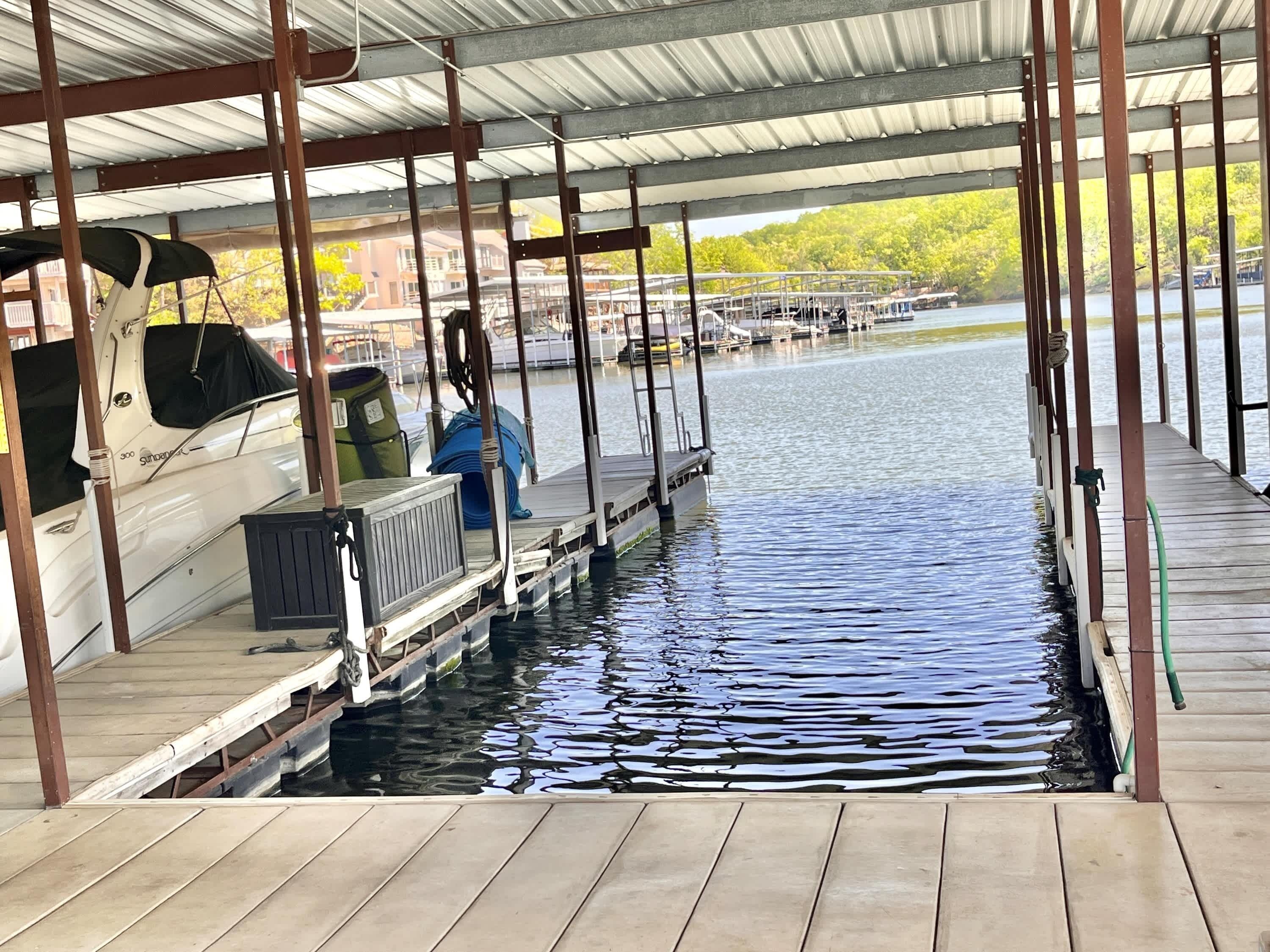 A covered dock with a boat moored on the left, a green hose, and a metal railing.