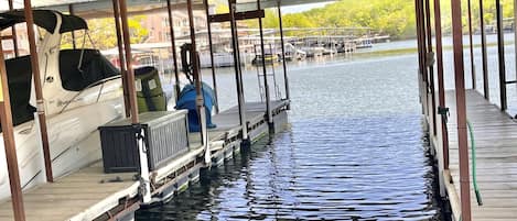 A covered dock with a boat moored on the left, a green hose, and a metal railing.