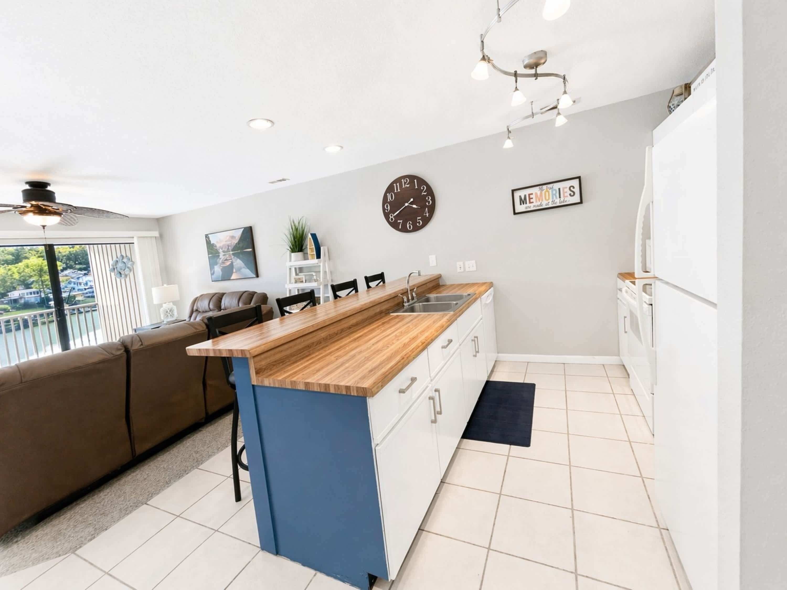 A modern kitchen with a wooden island, white cabinets, a clock, and a 'Memories' sign.