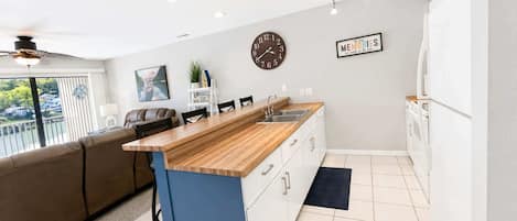 A modern kitchen with a wooden island, white cabinets, a clock, and a 'Memories' sign.