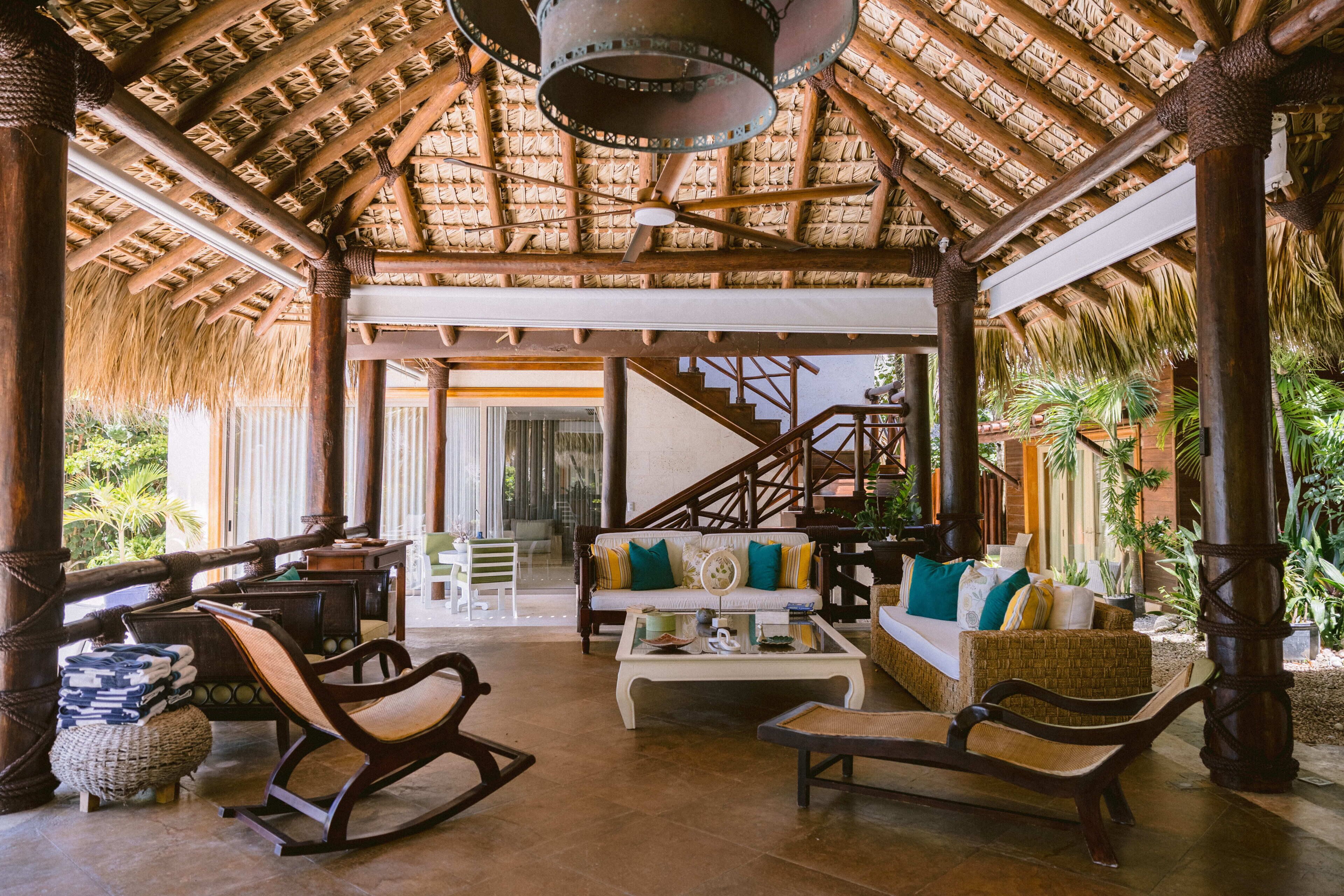 A spacious lounge area with a thatched roof, a sofa set, a coffee table, and a staircase leading to an upper level.