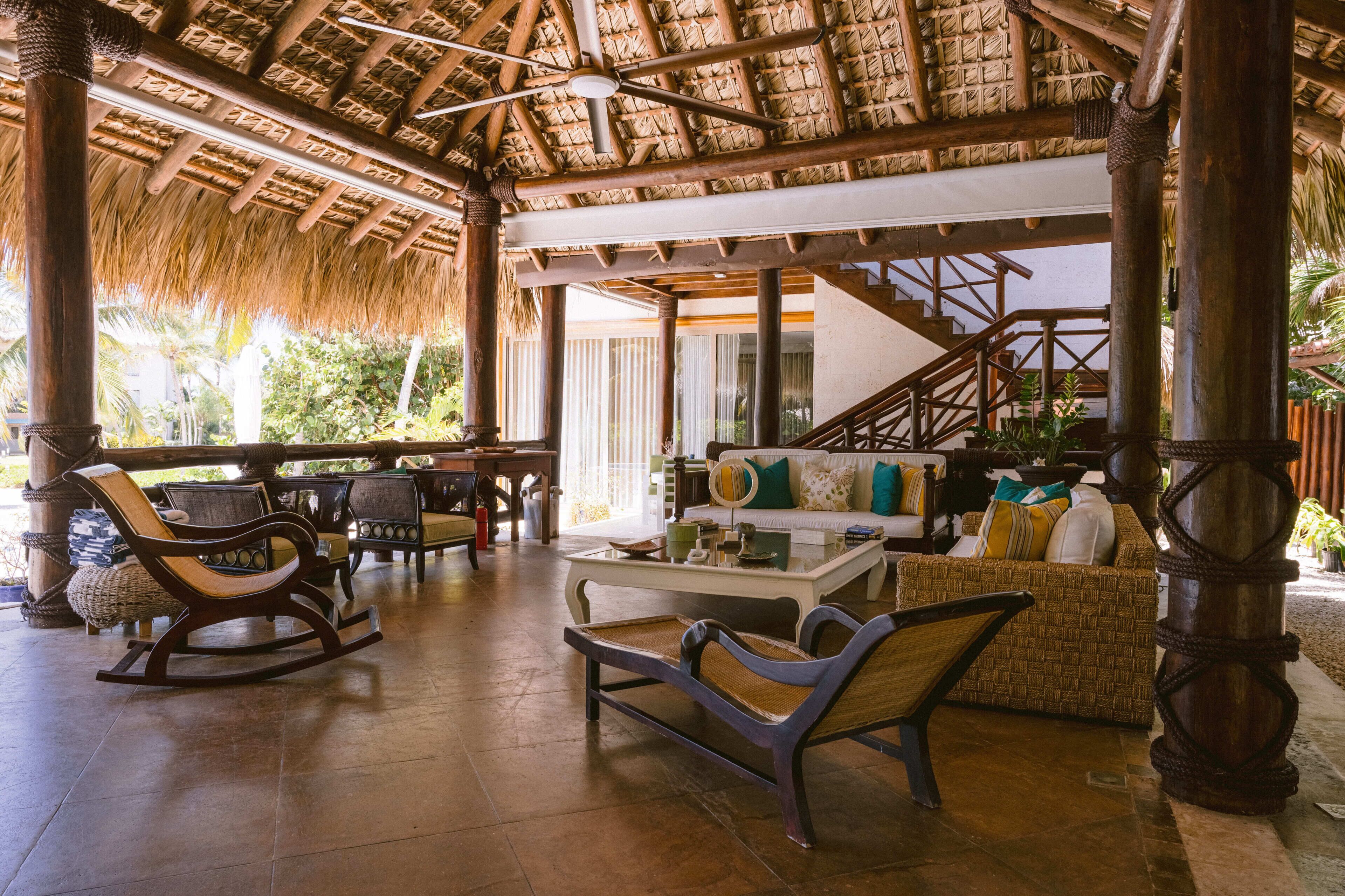 A covered outdoor lounge area with wicker furniture, a staircase, and a view of the outdoors.