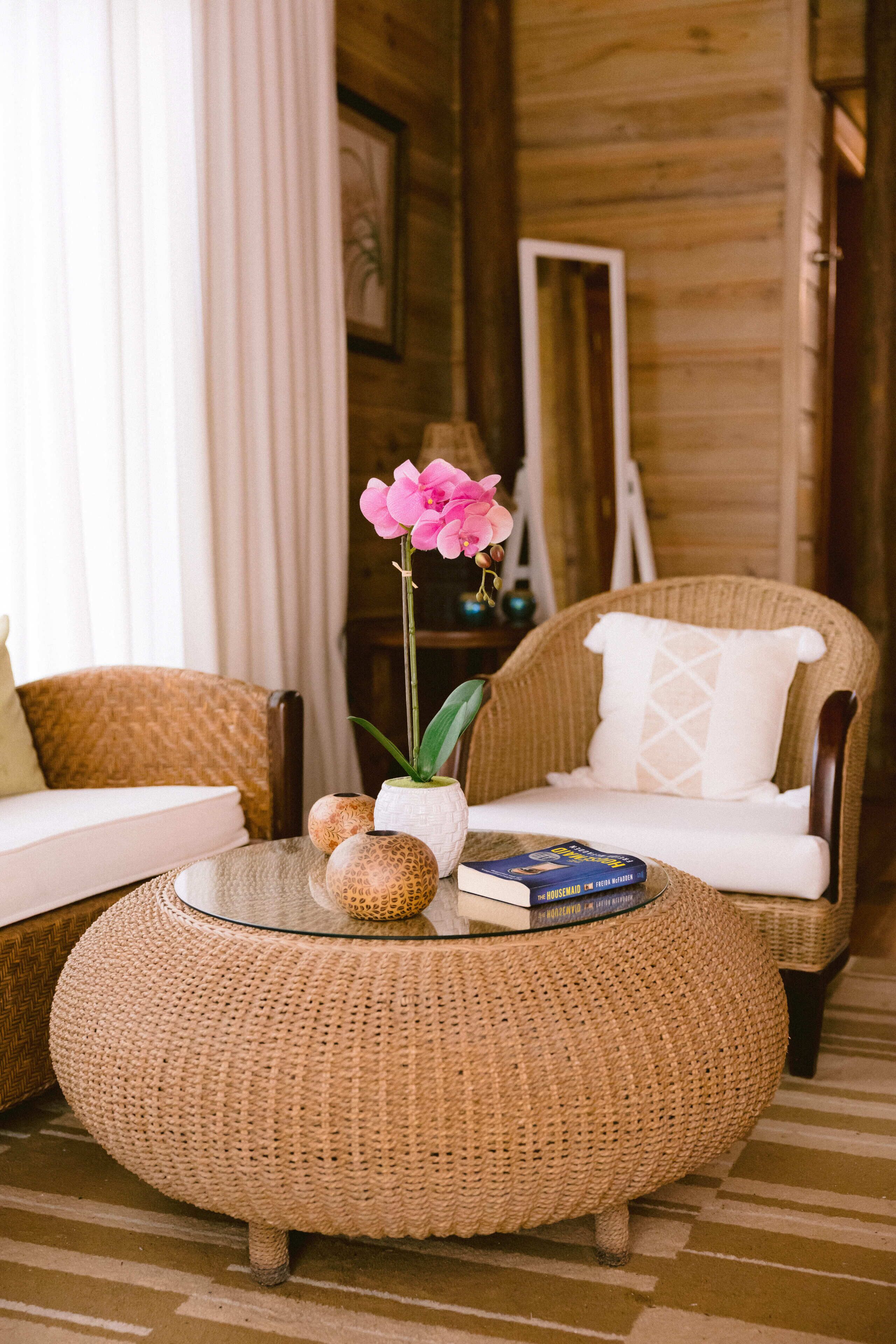 A cozy room with wicker furniture, a round ottoman, a book, and decorative items.