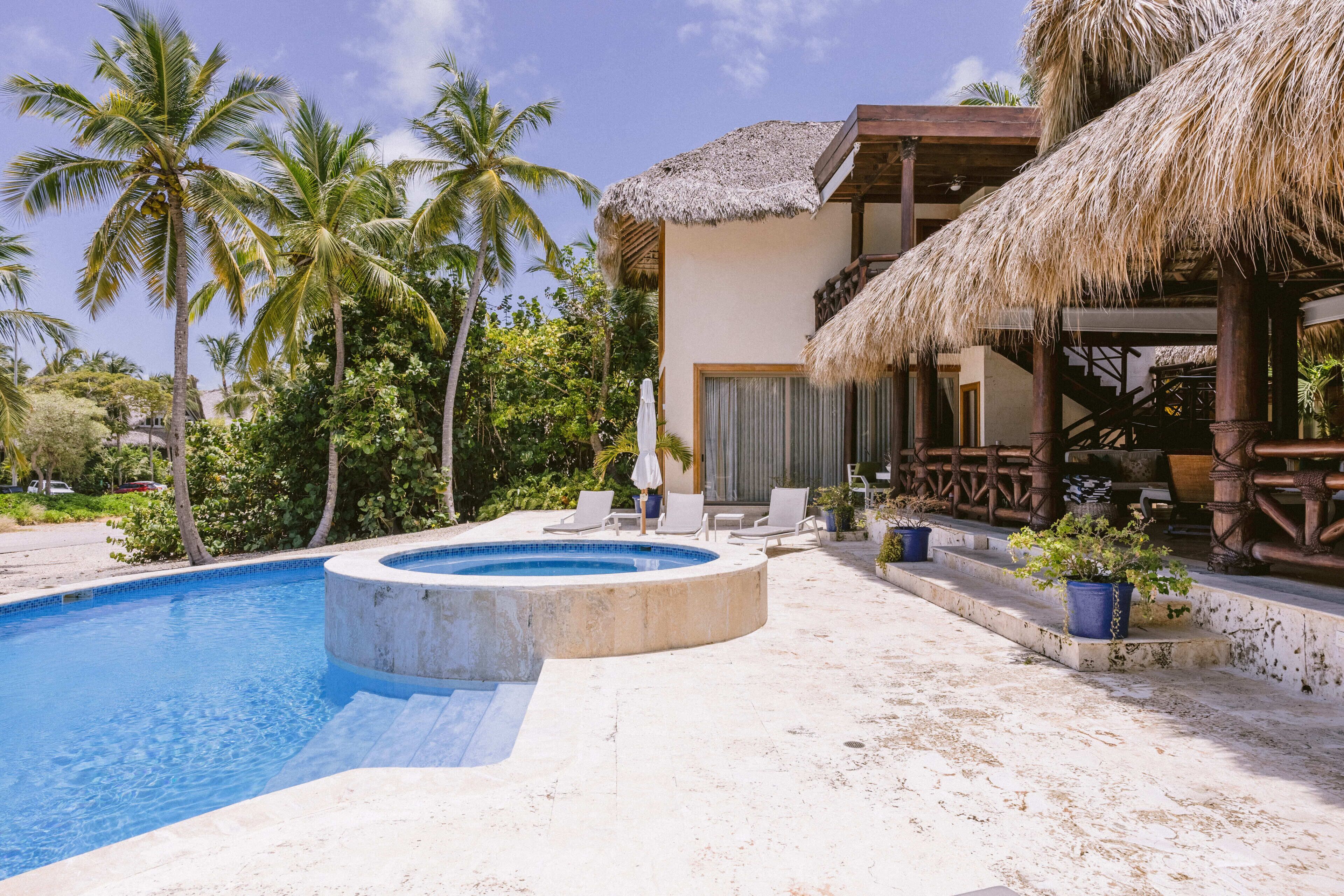 A pool area with a hot tub, lounge chairs, and a thatched-roof structure.