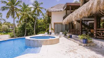 A pool area with a hot tub, lounge chairs, and a thatched-roof structure.