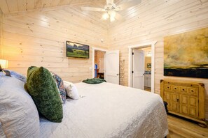 A room with a bed, a wooden headboard, a painting, and a ceiling fan. - Blue Water Pines · New! Heated Pool · Ping Pong, Hot Tub and Fire Pit (Broken Bow)