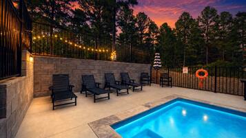Lounge poolside under string lights as the sky fades from orange to deep purple.