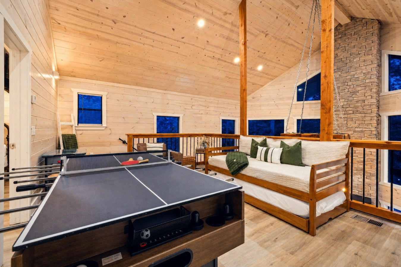 Ein Zimmer mit Tischtennisplatte, einem Bett mit Hängesitz und einer Ziegelwand.