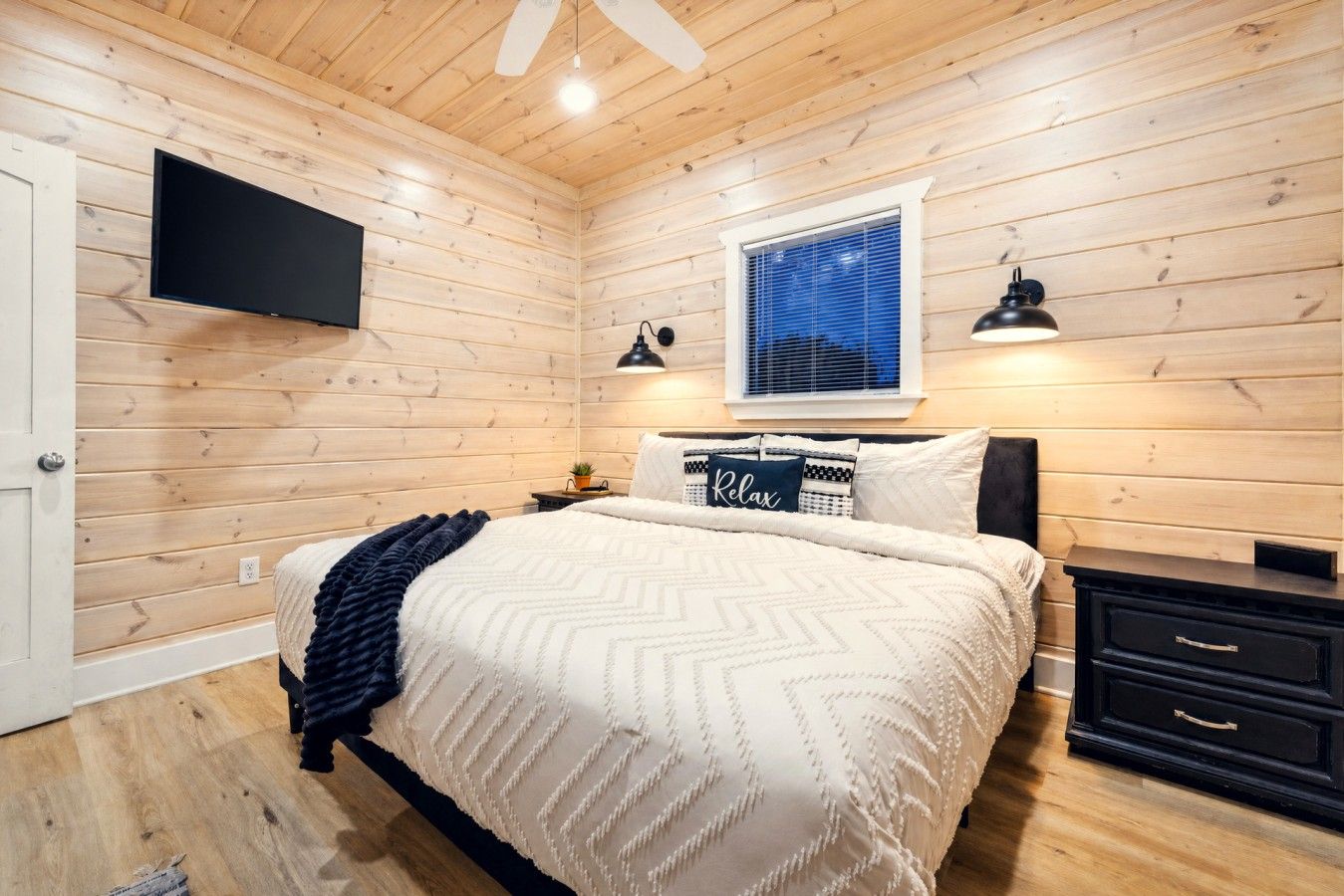 A bedroom with a bed, bedside tables, a TV, and a window with blinds.
