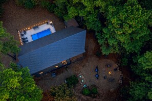 An aerial view of a property with a large building, a swimming pool, and outdoor seating. - Blue Water Pines · New! Heated Pool · Ping Pong, Hot Tub and Fire Pit (Broken Bow)