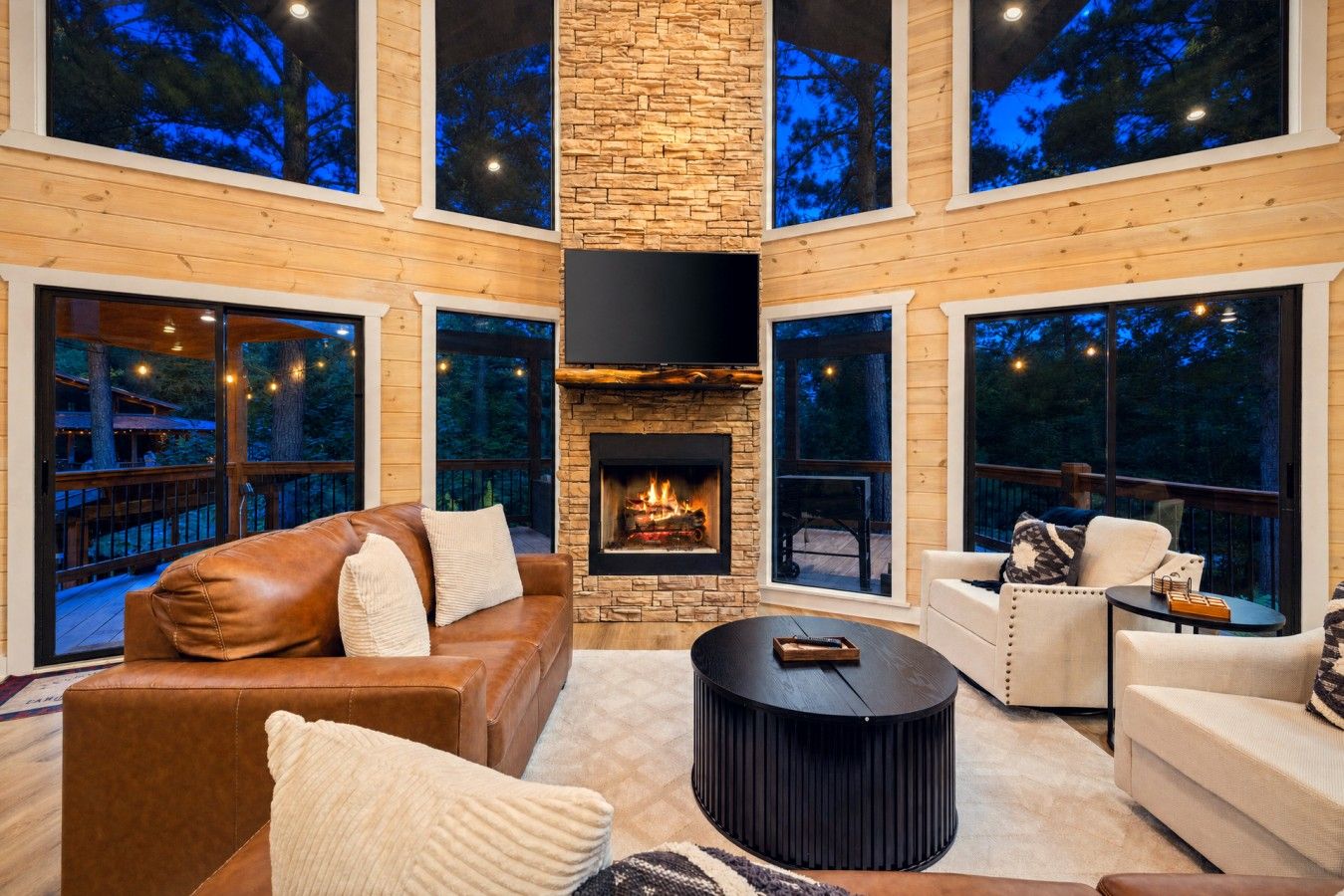 A spacious living room with a stone fireplace, leather sofas, and large windows offering views of the outdoors.