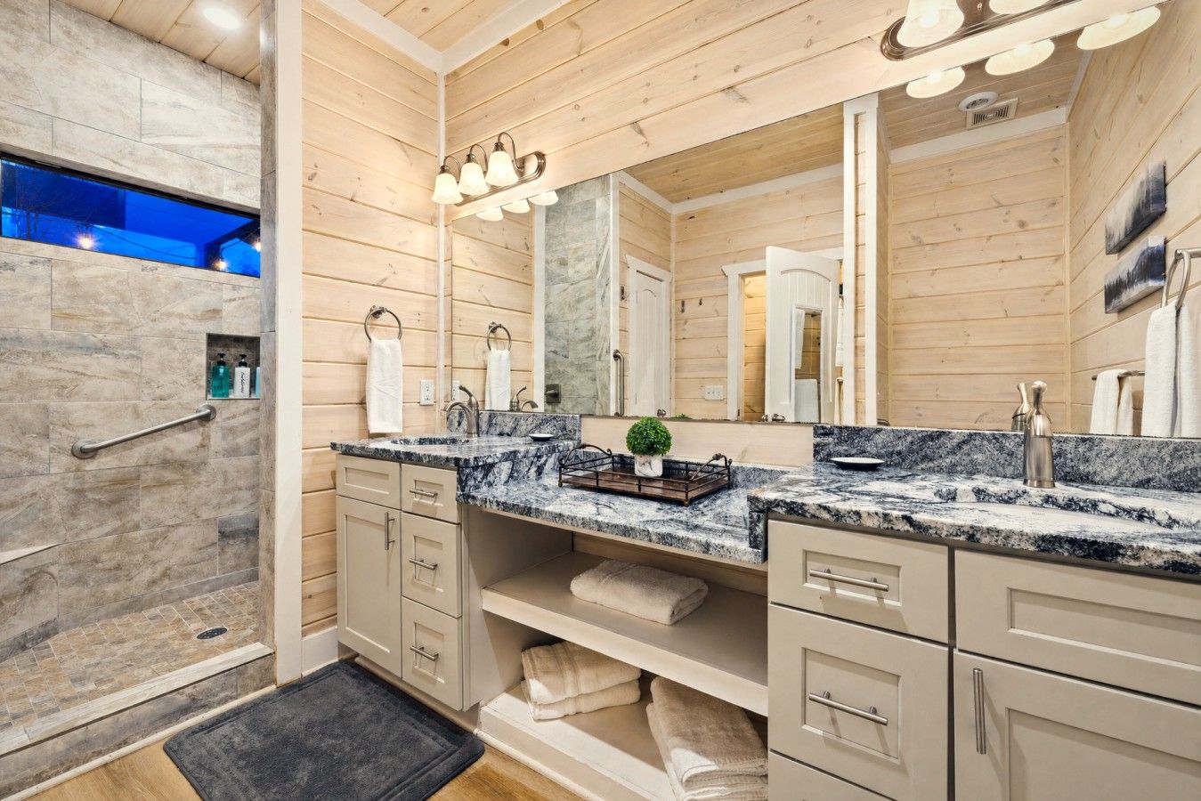 Ein Badezimmer mit Dusche, Marmorplatte, Holztisch und einem großen Spiegel.
