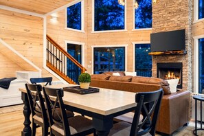 A modern interior with a fireplace, wooden walls, and a staircase. - Blue Water Pines · New! Heated Pool · Ping Pong, Hot Tub and Fire Pit (Broken Bow)