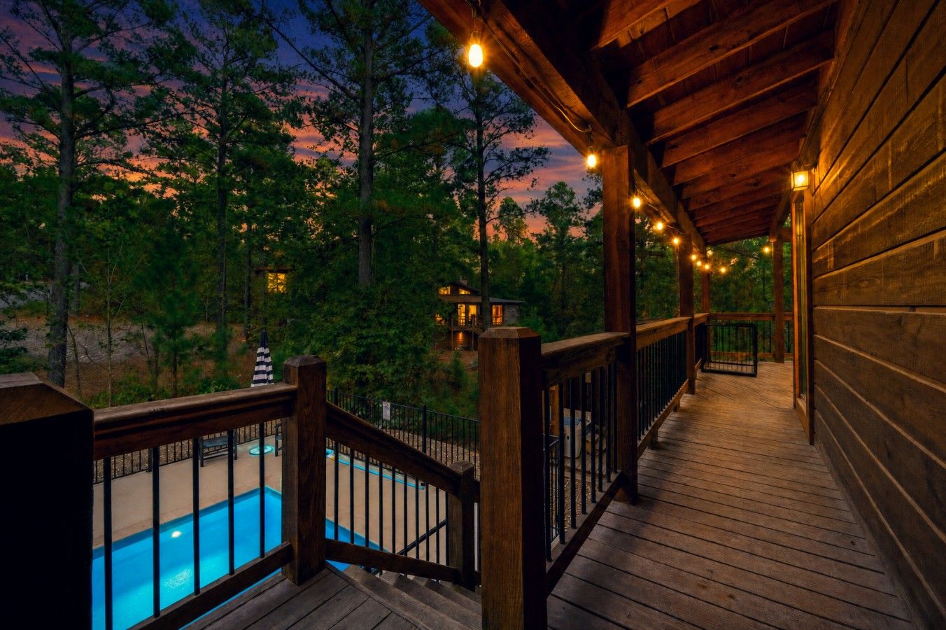 A wooden deck with a pool, surrounded by trees and a sunset view.
