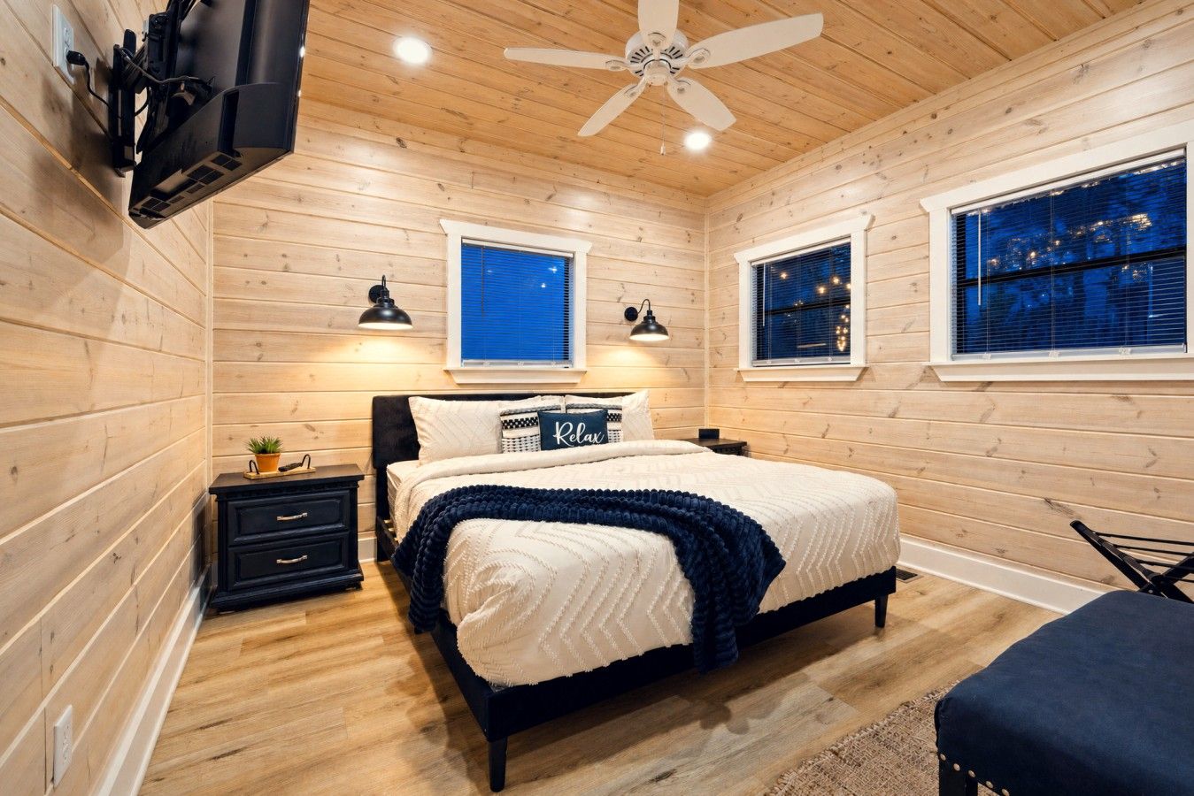 A bedroom with a bed, bedside tables, a ceiling fan, and windows.