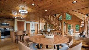 Un intérieur spacieux en bois, avec une table de salle à manger ronde, des tabourets de bar, un escalier et un coin cuisine.