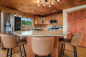 Cocina con armarios de madera, encimera de granito, electrodomésticos de acero inoxidable y una barra con taburetes.