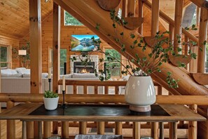 Un interior de madera con chimenea, un televisor mostrando una vista panorámica y un comedor con mesa y sillas.