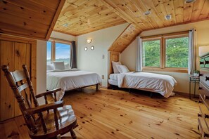Una habitación con pisos de madera, dos camas con ropa blanca, una silla de madera y un aparador.